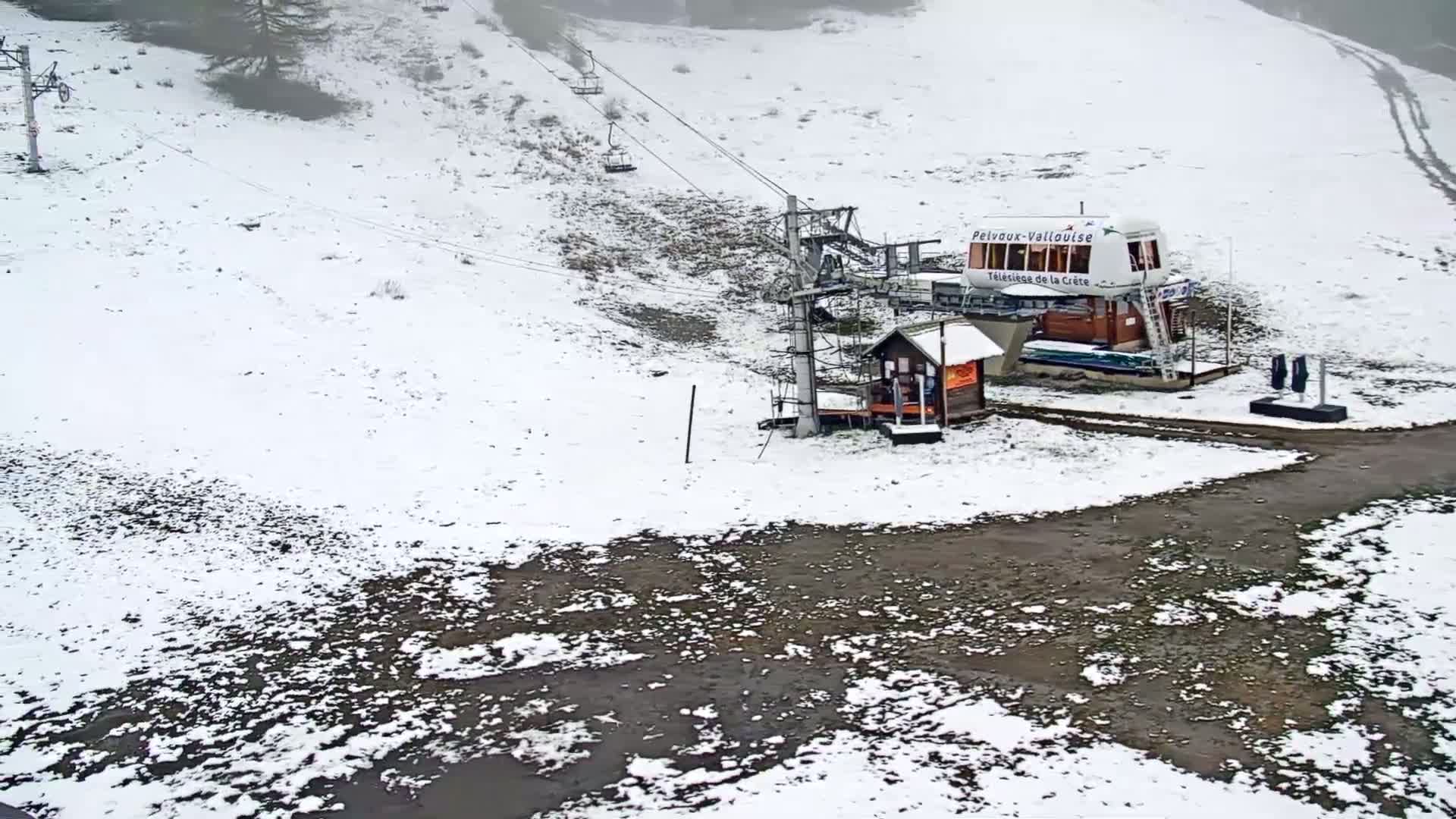 A ski lift station sits on a snow-covered hillside with a partially snow-covered ground area near the base of the lift.