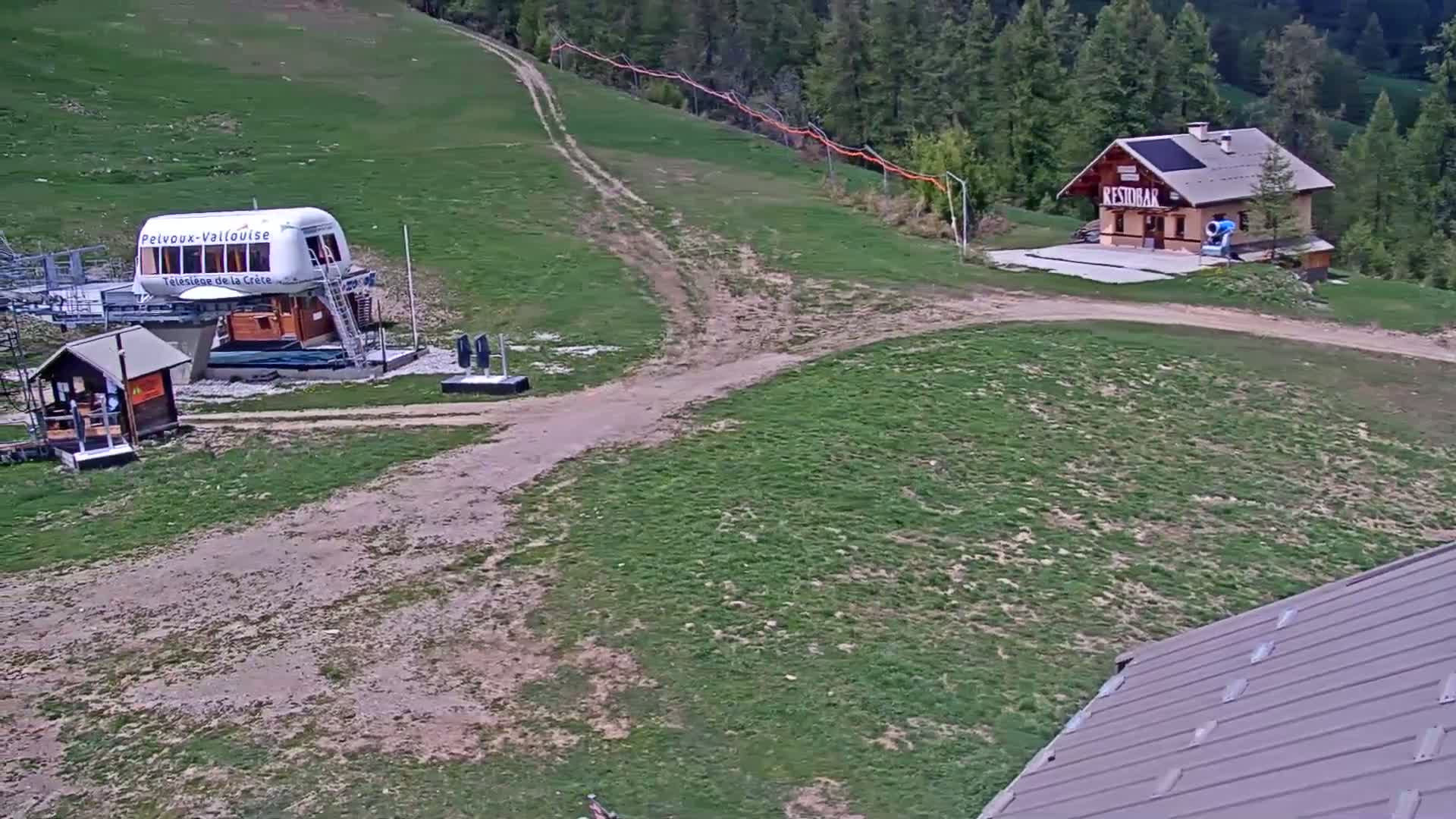 A chairlift and small building sit on a grassy hillside with a dirt path leading to them, under sunny skies.