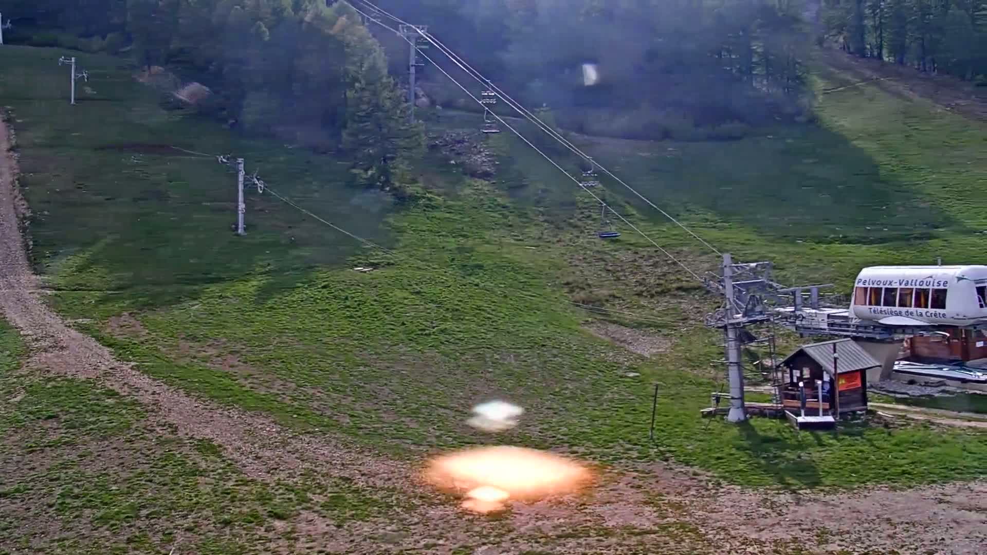 A chairlift station sits on a grassy hillside with a dirt path, under hazy conditions.