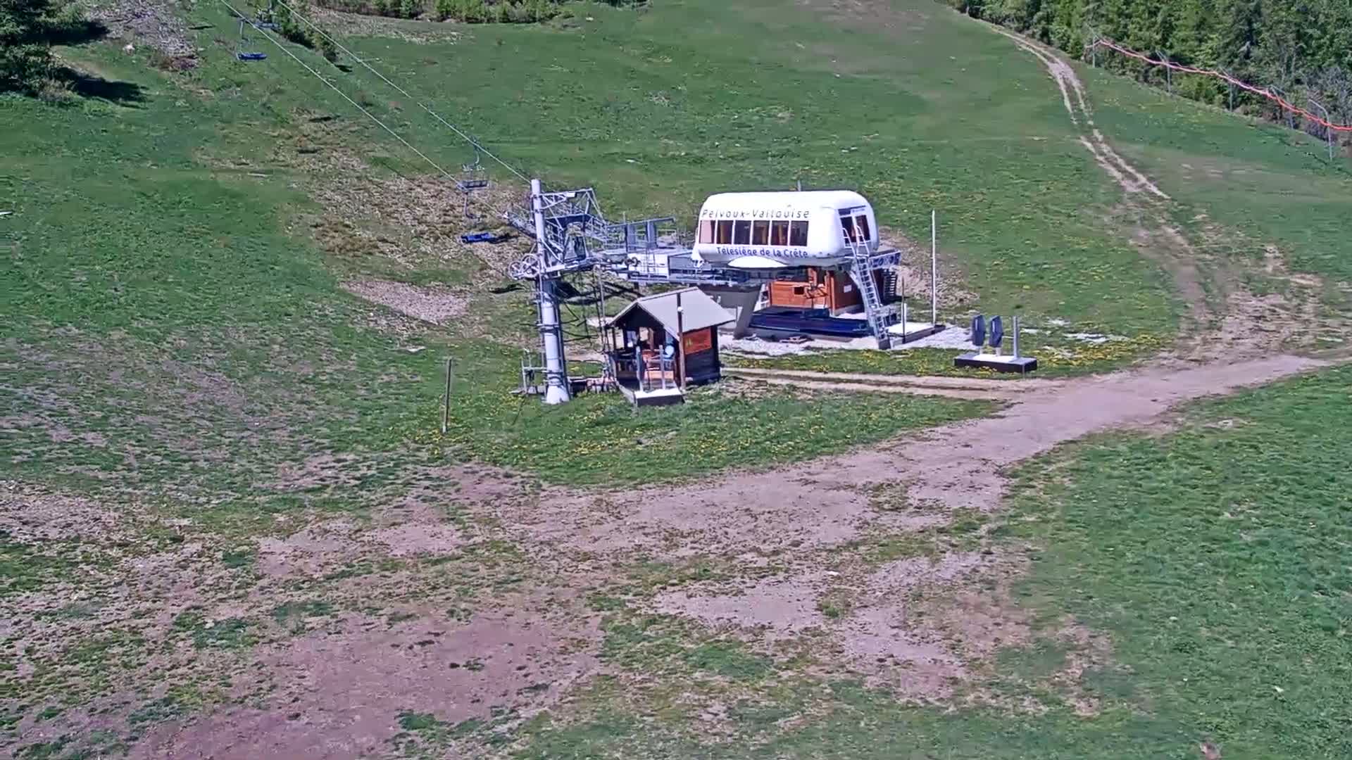 A chairlift station sits atop a grassy hill on a sunny day.