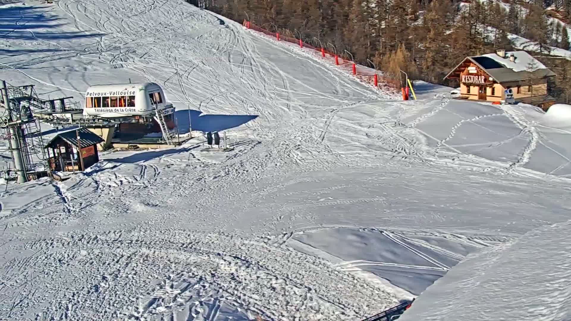 A snow-covered forest of coniferous trees ascends a mountain alongside a deep snowy slope with faint ski tracks, all under a grey, overcast sky, with a small, partially snow-buried red-roofed hut visible at the bottom.
