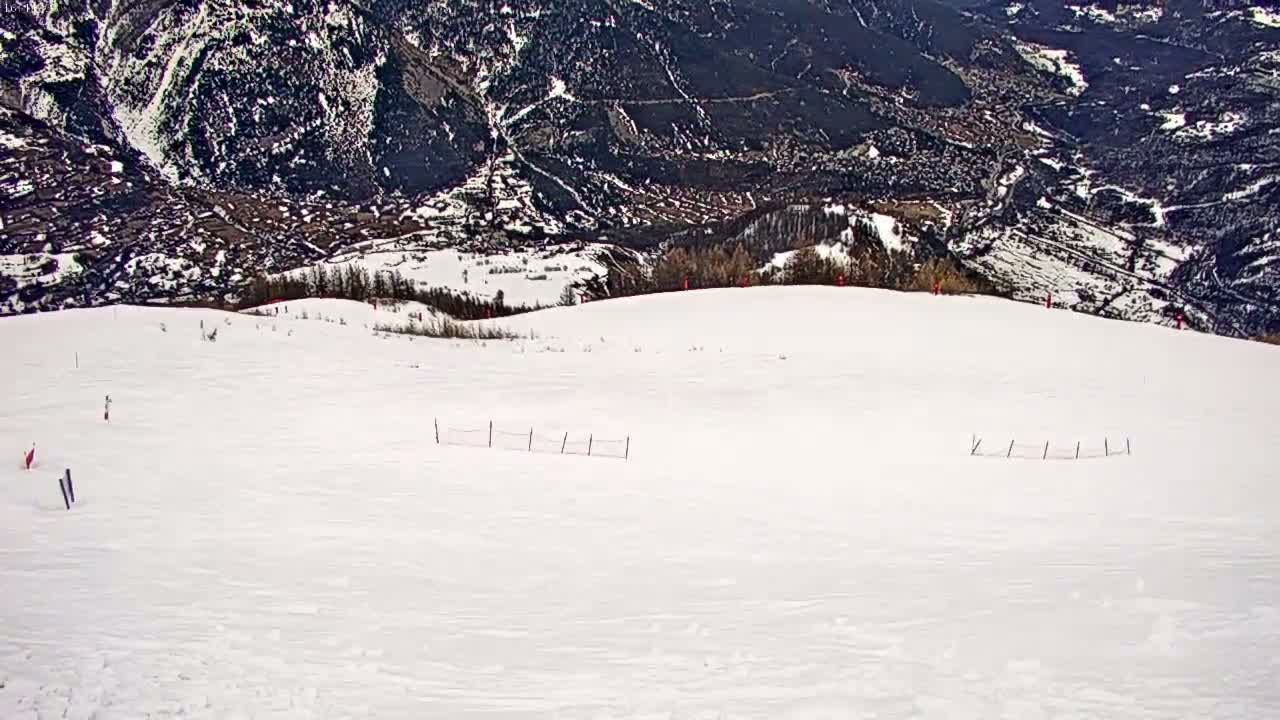 A snow-covered ski slope overlooks a mountainous valley under a clear sky.