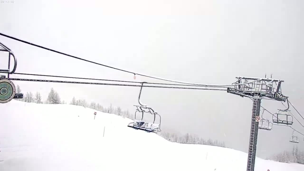 A snow-covered ski lift ascends a snowy hillside under an overcast sky.