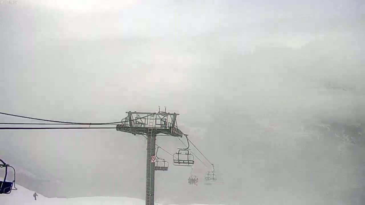 A ski lift with several occupied chairs ascends through a heavy fog or snowstorm.