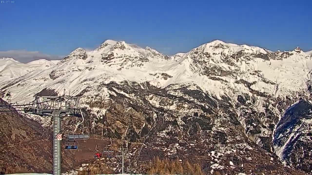 A ski lift ascends a mountain range covered in snow under a clear blue sky.