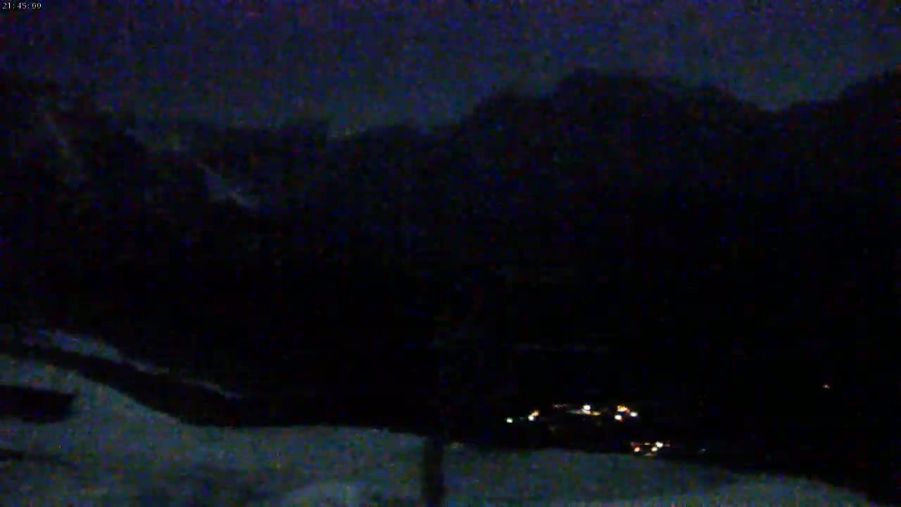 A nighttime view of dark mountains and a small village with scattered lights in the valley below.