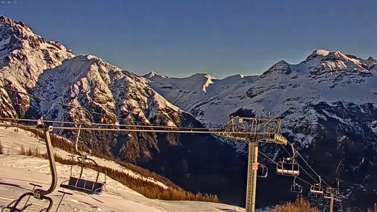 A chairlift ascends a snowy mountain range under a clear blue sky.