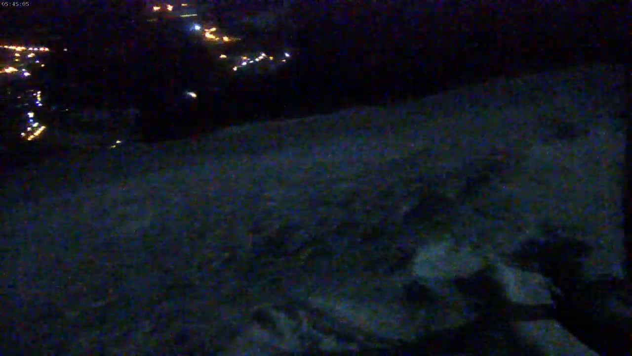 A dark, snow-covered landscape is visible at night, with distant lights illuminating a town or village in the background.