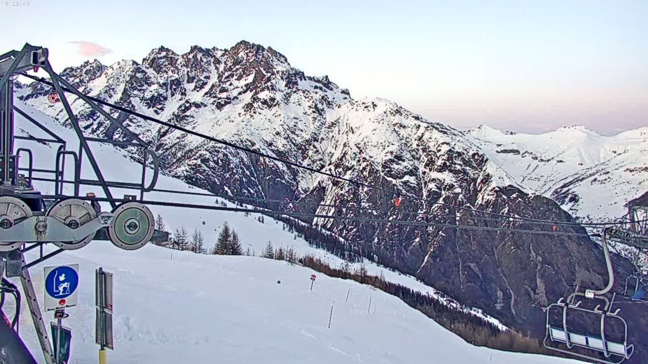 A snow-covered mountain range is viewed from a ski lift on a clear, bright day.