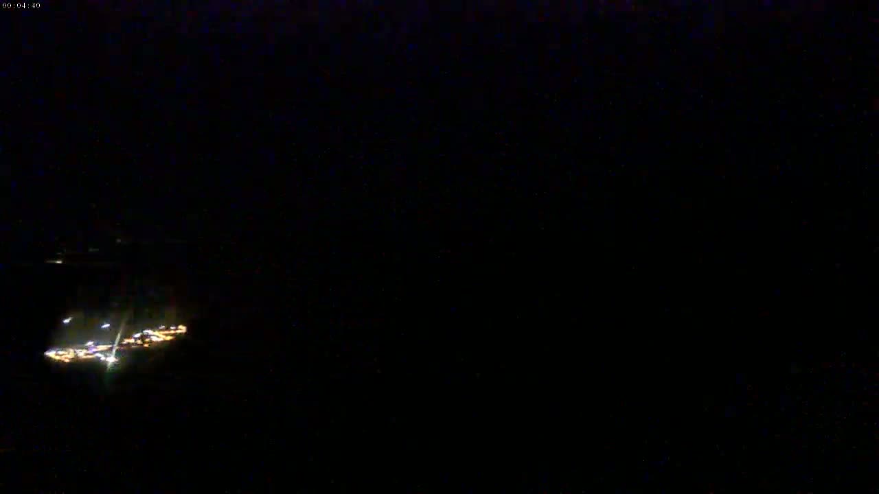 A low-light nighttime image shows a small cluster of illuminated structures in the distance.