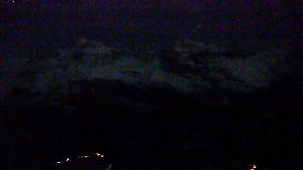 A nighttime, low-light view shows a dark landscape with faint clouds and a few distant lights.