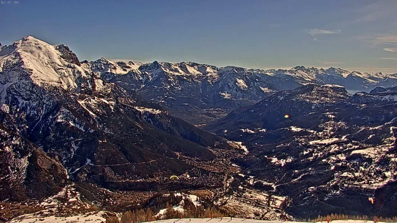 A snow-capped mountain range stretches into a valley under a clear blue sky, with a small town nestled within the valley below.