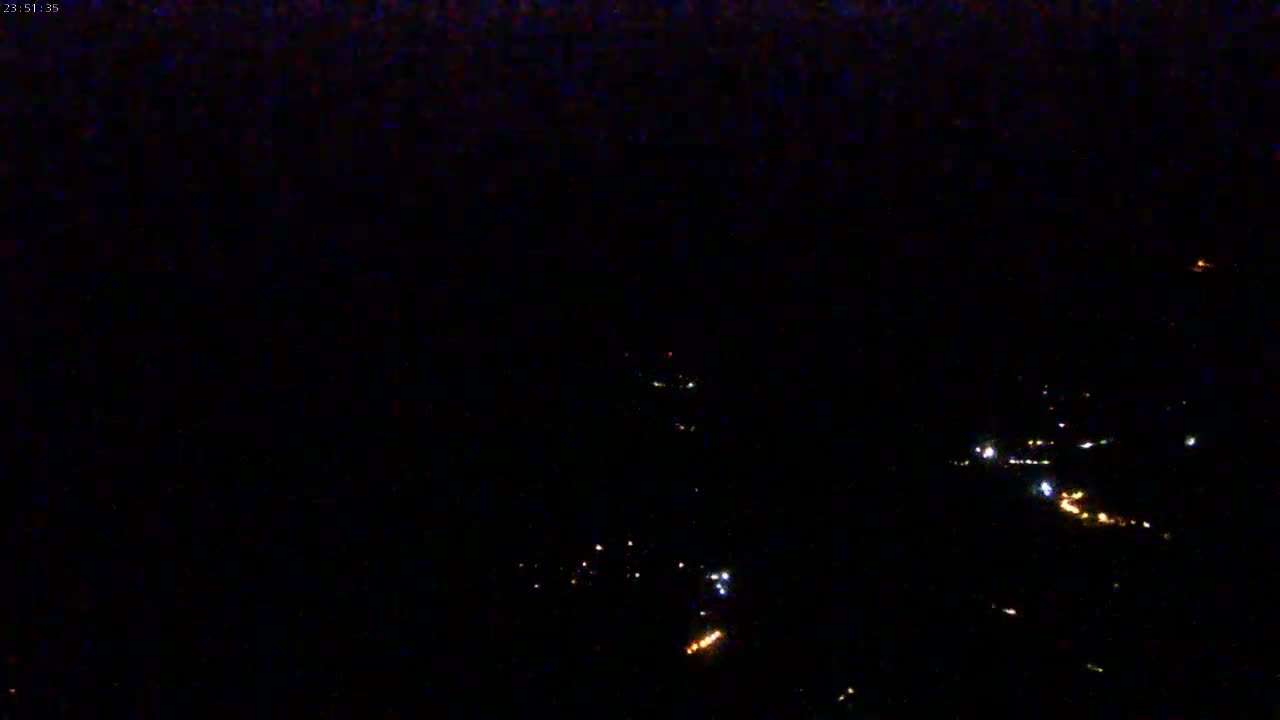 A nighttime aerial view shows a scattering of faint lights on the ground under a dark sky.