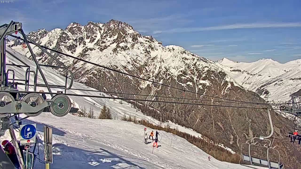A ski lift ascends a snowy mountain range under a clear blue sky.