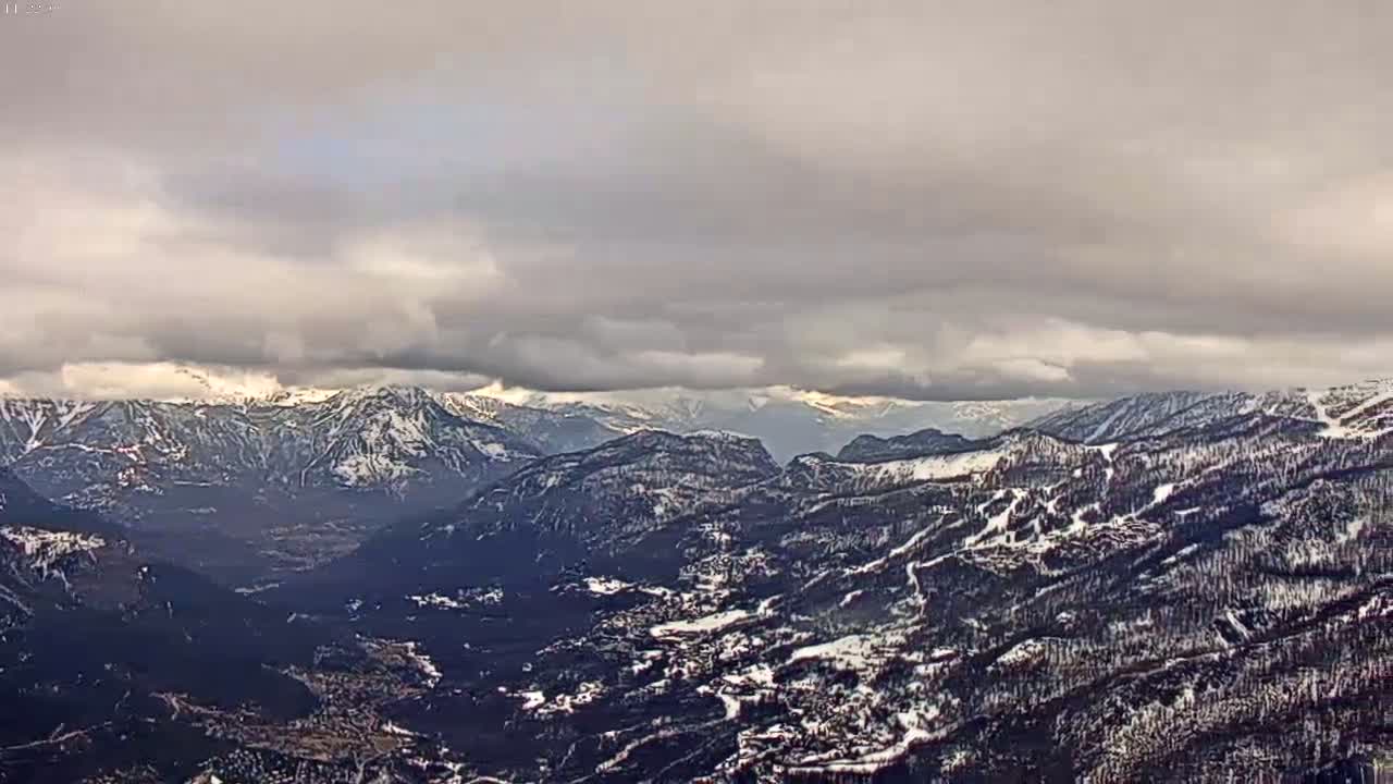 A snow-covered mountain valley is viewed under a cloudy sky.