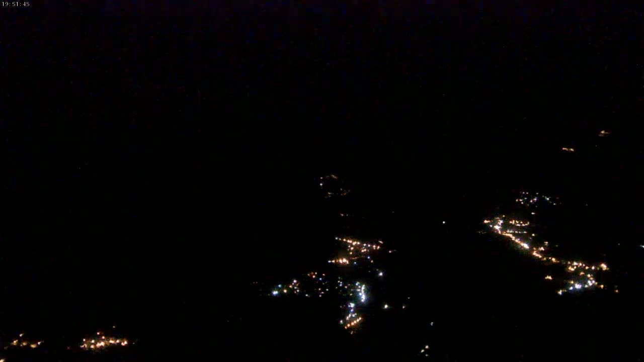 A nighttime aerial view shows scattered lights from a town or village below.