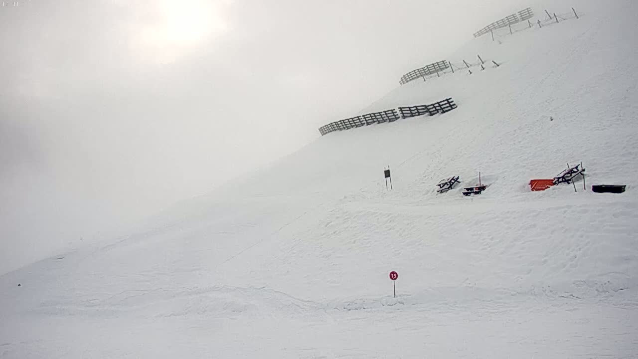 A snow-covered hill with a few picnic tables and fences is visible under foggy conditions.