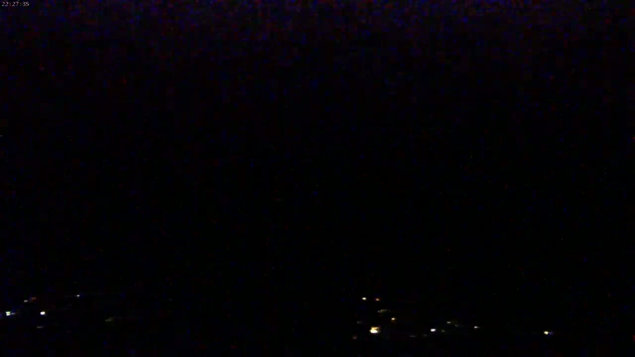 A nighttime, dark image shows a few small, faint lights in the distance at the bottom of the frame.