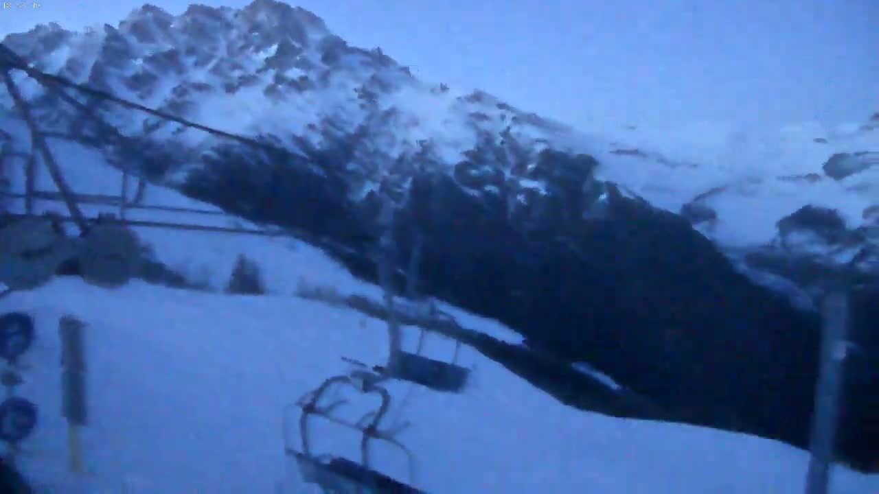 A snowy mountainside with a chairlift and empty chairs under a twilight sky.