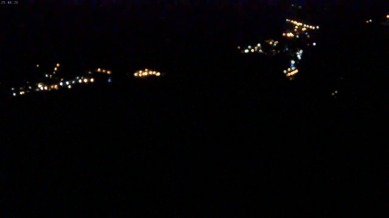 A dark nighttime scene shows blurry lights of a distant town or village.