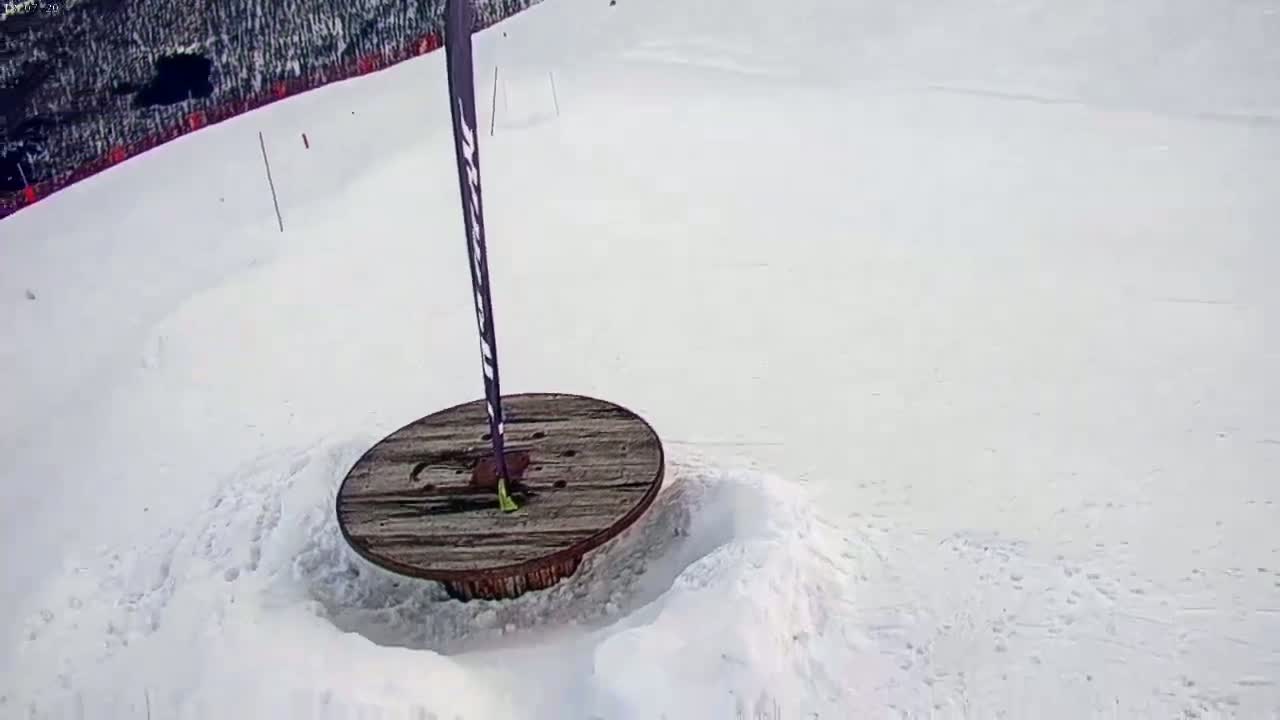 A wooden spool is partially buried in snow on a snow-covered slope, with a tall pole standing beside it.