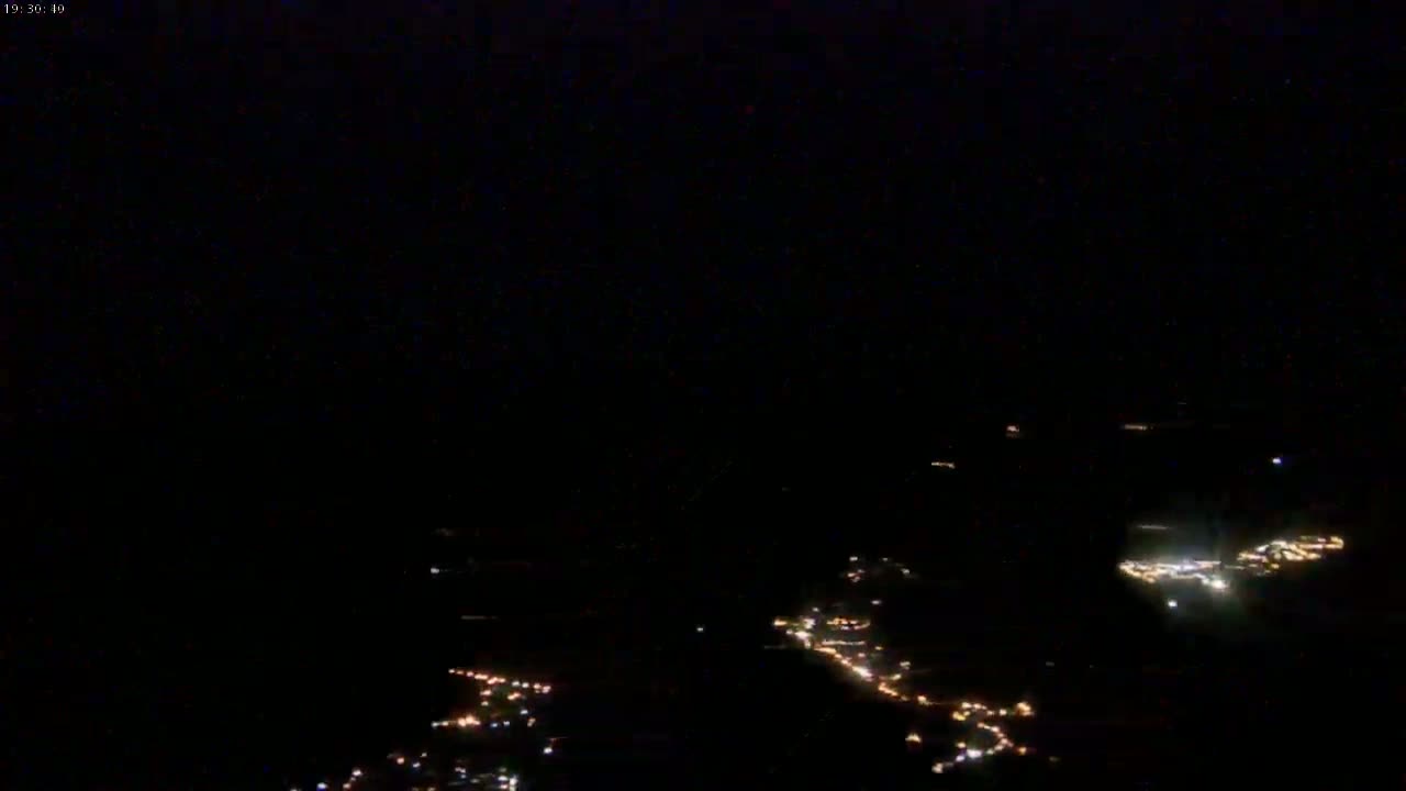 A nighttime aerial view shows scattered clusters of small, faint lights against a completely dark sky.