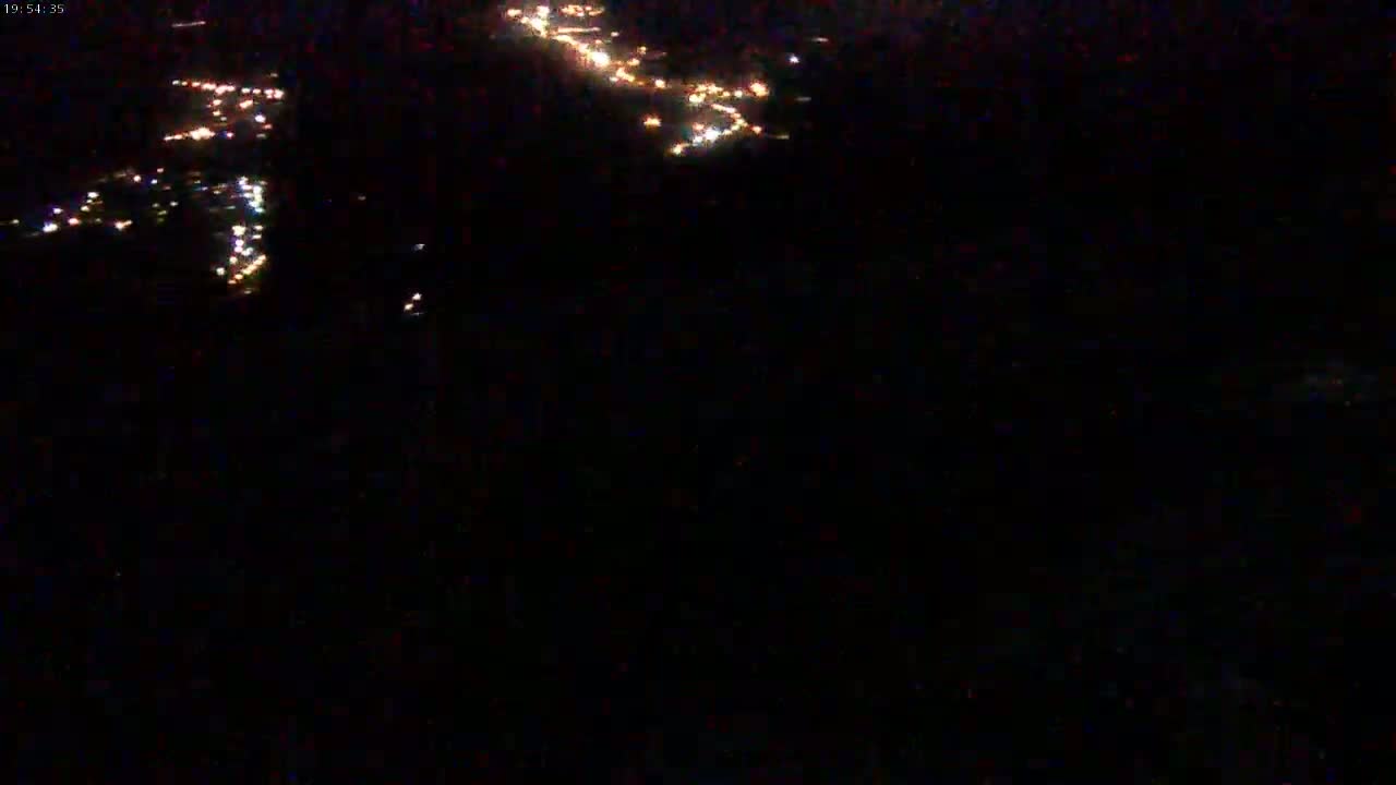 A nighttime aerial view shows scattered points of light, likely from a city or town, under a dark sky.