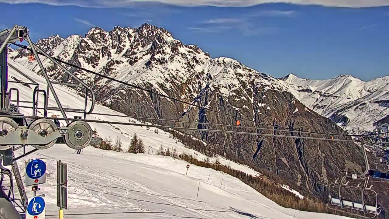 A ski lift chair ascends a snowy mountain slope under a mostly clear blue sky.