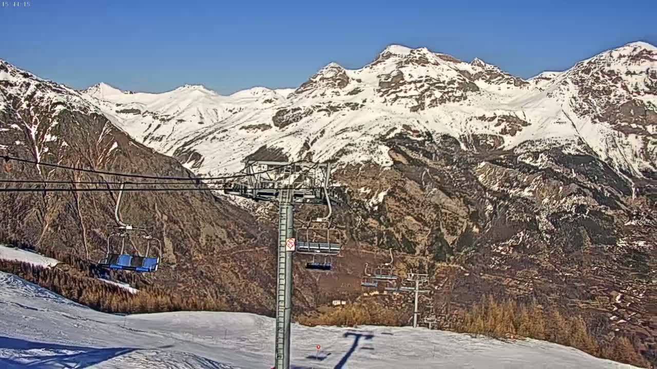A chairlift ascends a snowy mountain range on a clear, sunny day.
