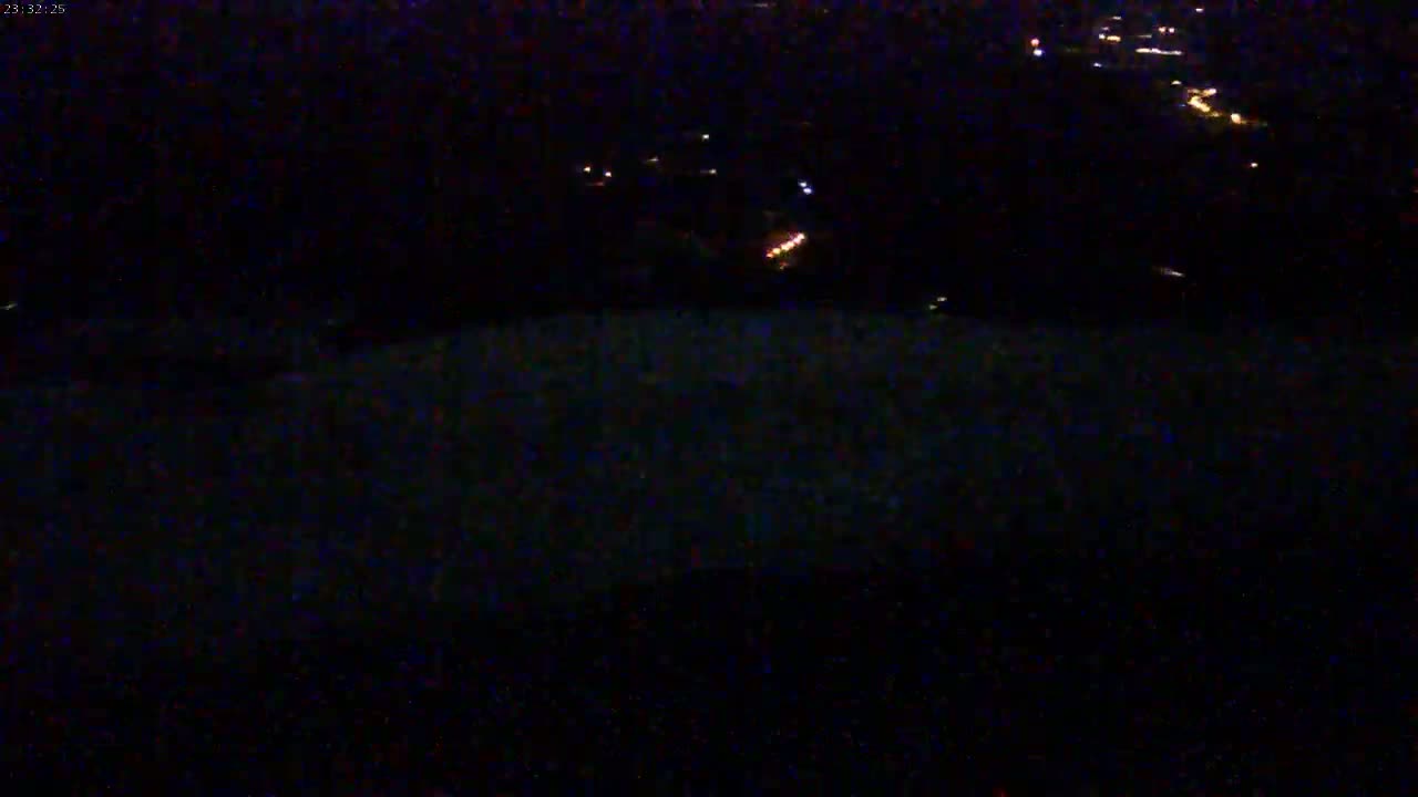 A nighttime, high-angle view shows a dark landscape with a few distant, faint lights.