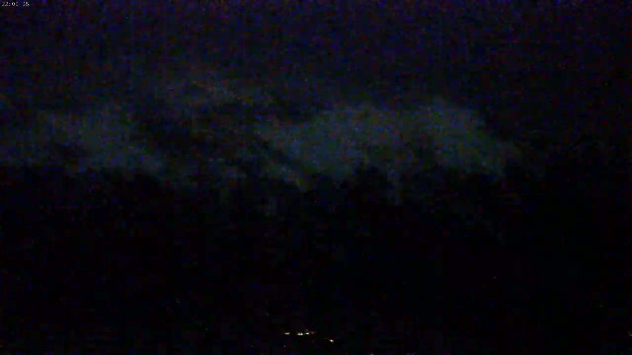 A nighttime view shows dark clouds illuminated from below by faint lights on the ground.