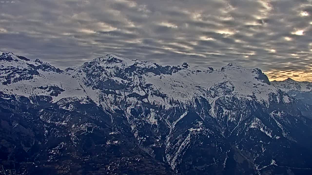 A snow-capped mountain range is visible under a cloudy sky with hints of sunrise or sunset.