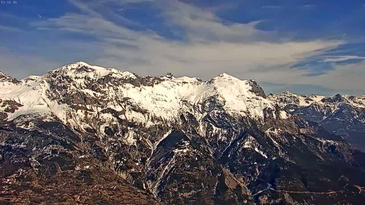 A snow-capped mountain range stretches across a clear, partly cloudy sky.