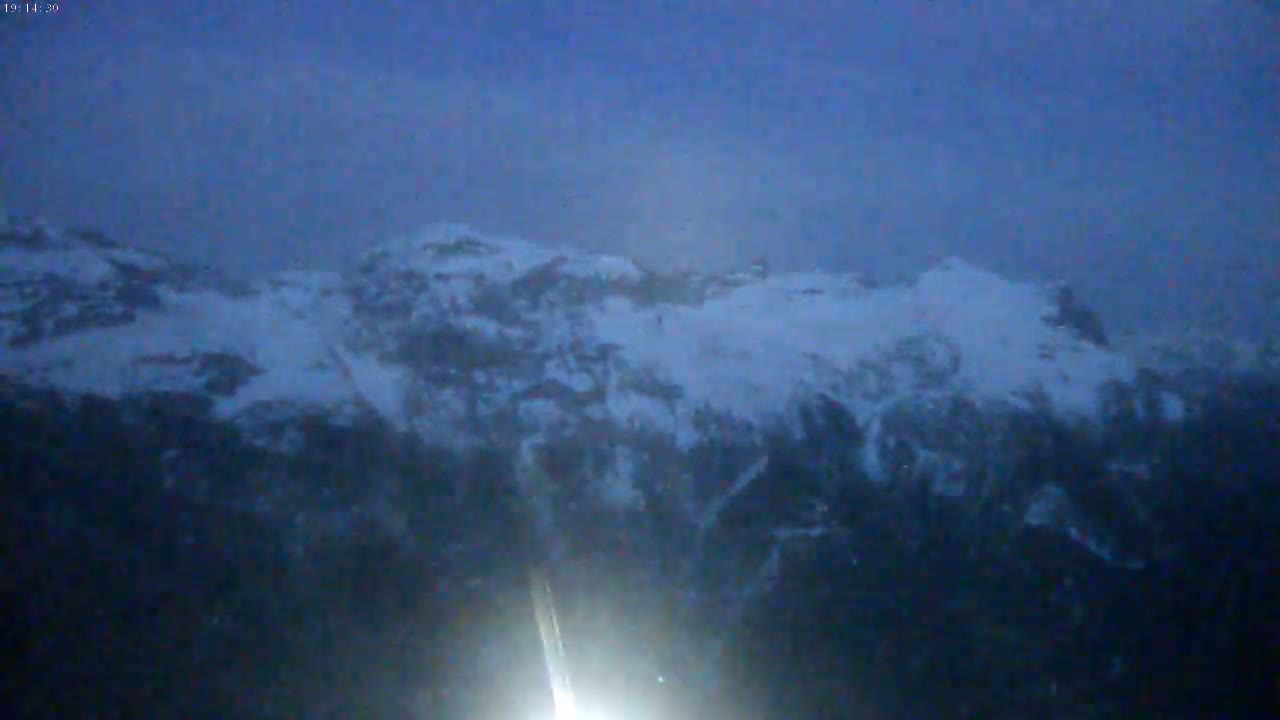 A snow-covered mountain range is visible in the dusky light of either dawn or dusk, with a bright light source in the foreground.