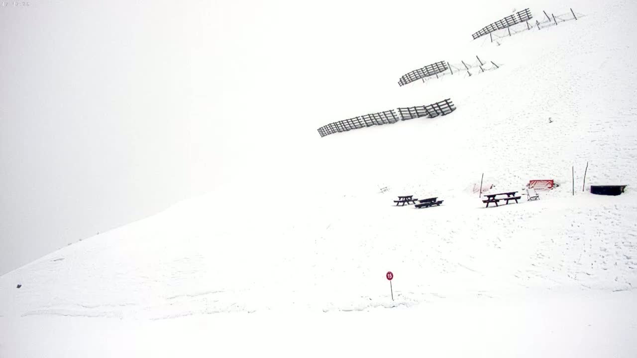 A snow-covered hillside with several picnic tables and snow fences under overcast skies.