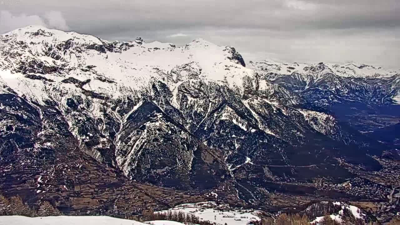 A snow-covered mountain range stretches into a valley under a cloudy sky.