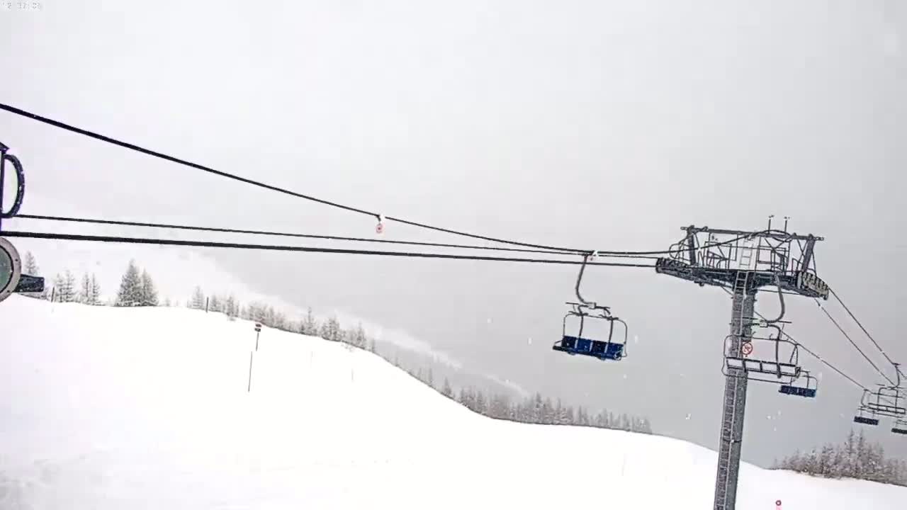 A snow-covered ski slope is visible from a chairlift during a snowstorm.