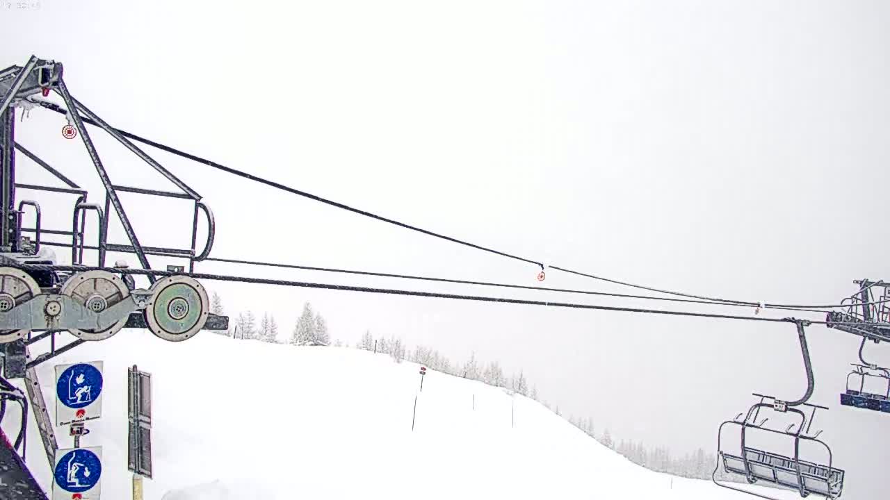 A chairlift extends across a snow-covered ski slope in snowy conditions.