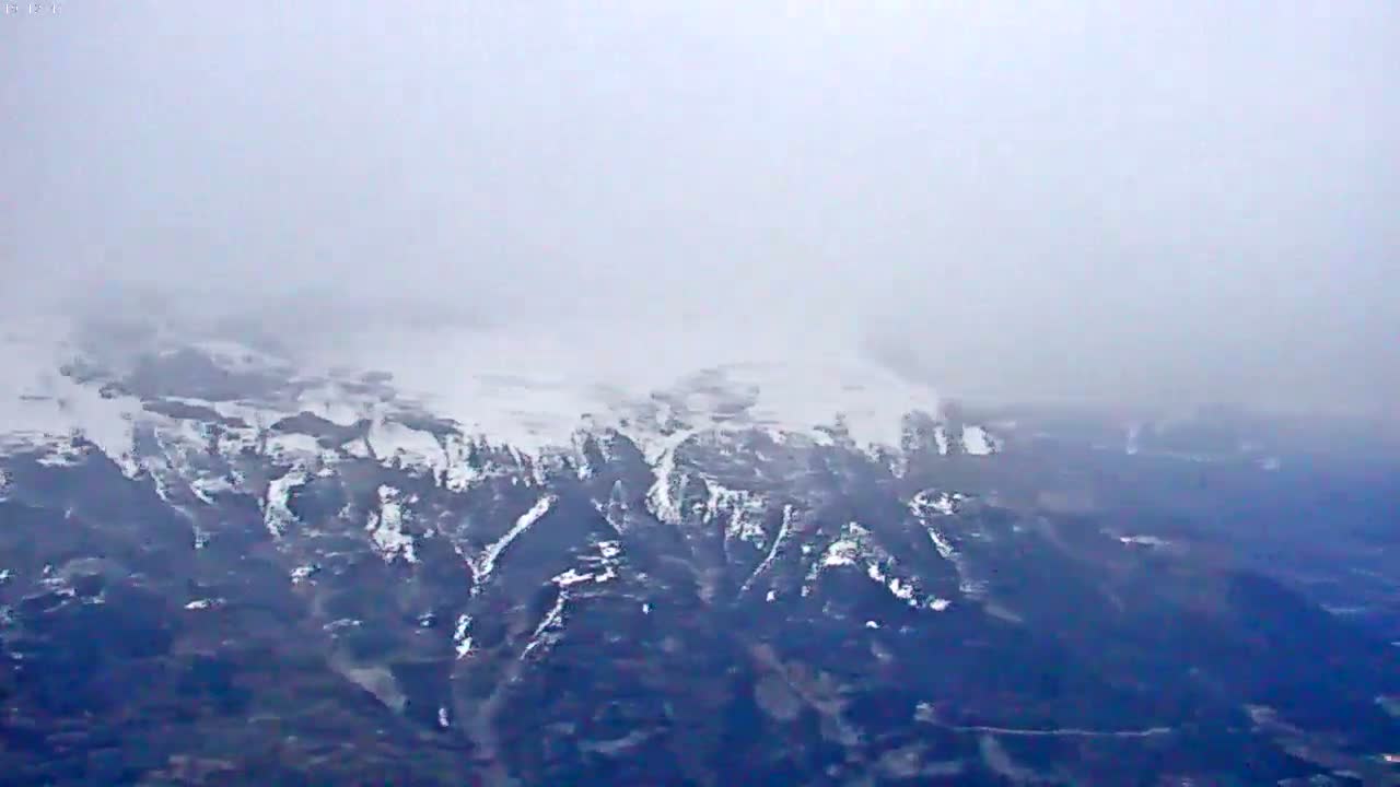 A snow-covered mountain range is partially obscured by fog or mist.