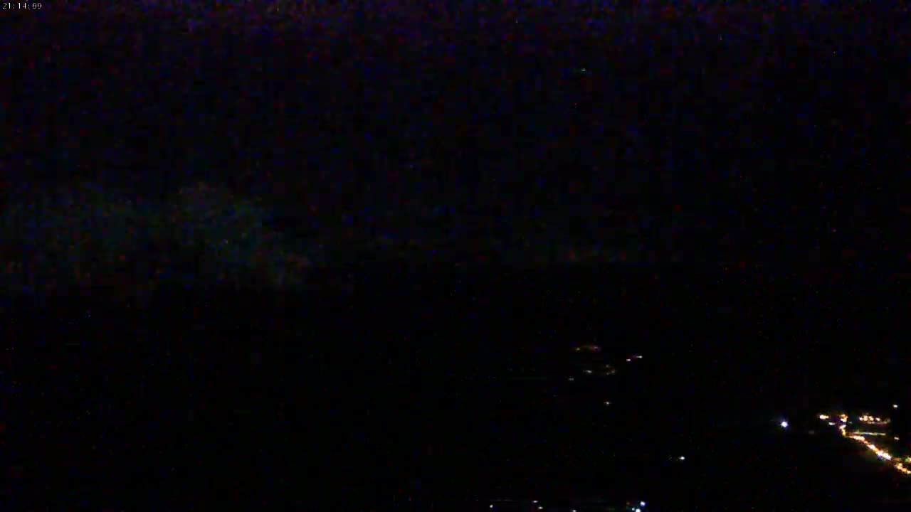 A nighttime, long-distance view shows a dark sky with faint, distant lights below.