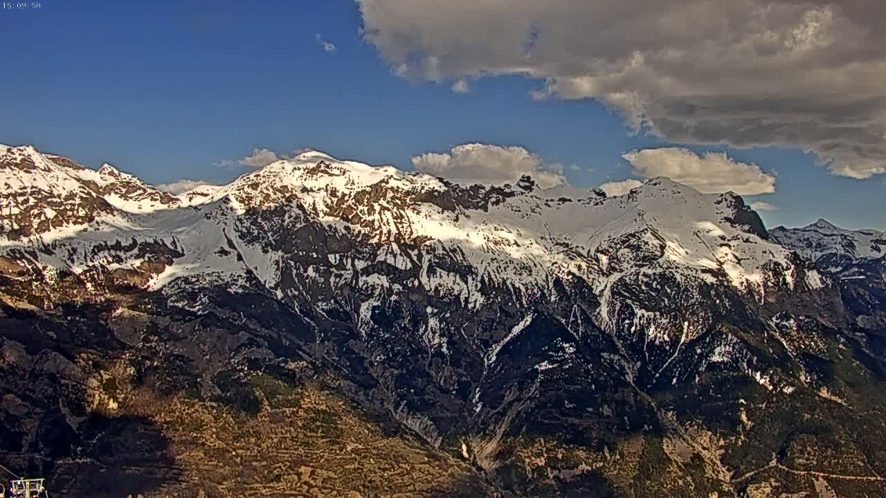 A partly cloudy day reveals a snow-capped mountain range, with lower slopes showing dark vegetation.