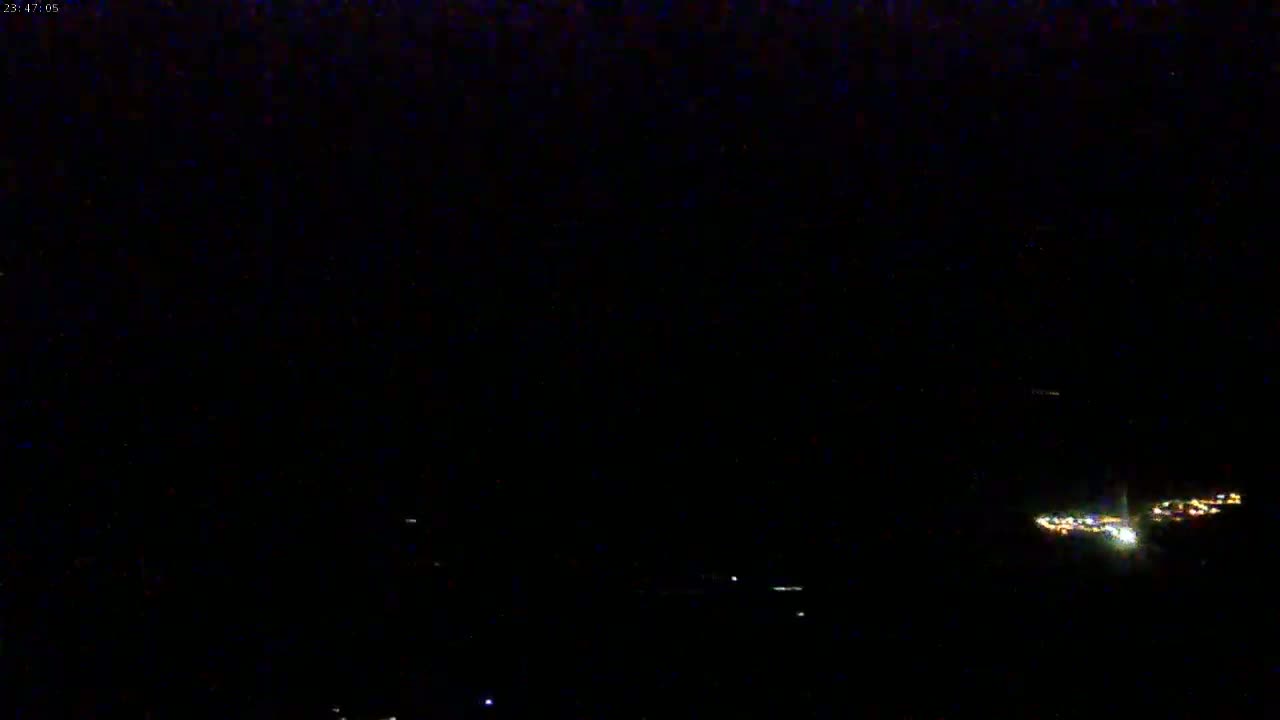 A nighttime, low-light image shows a few distant clusters of lights on a dark horizon.