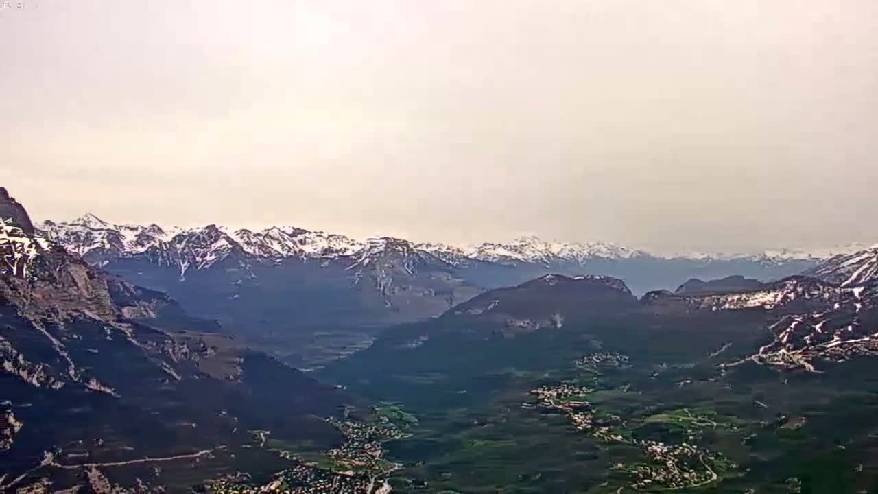 A hazy, high-angle view shows a valley nestled between snow-capped mountains.