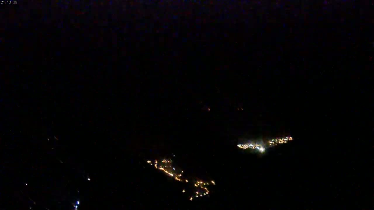A nighttime aerial view shows two clusters of small, scattered lights below in the darkness.