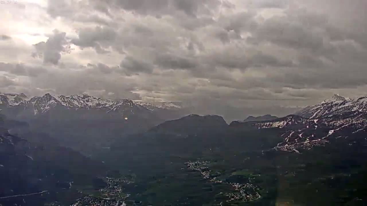 A vast, mountainous landscape stretches out under a cloudy, overcast sky, with snow visible on the highest peaks.