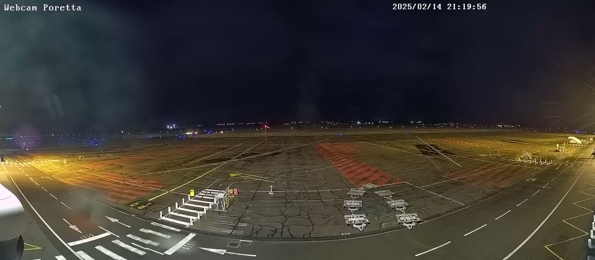 A nighttime view of an airport tarmac with several baggage carts, and a jetway, under a dark, clear sky.