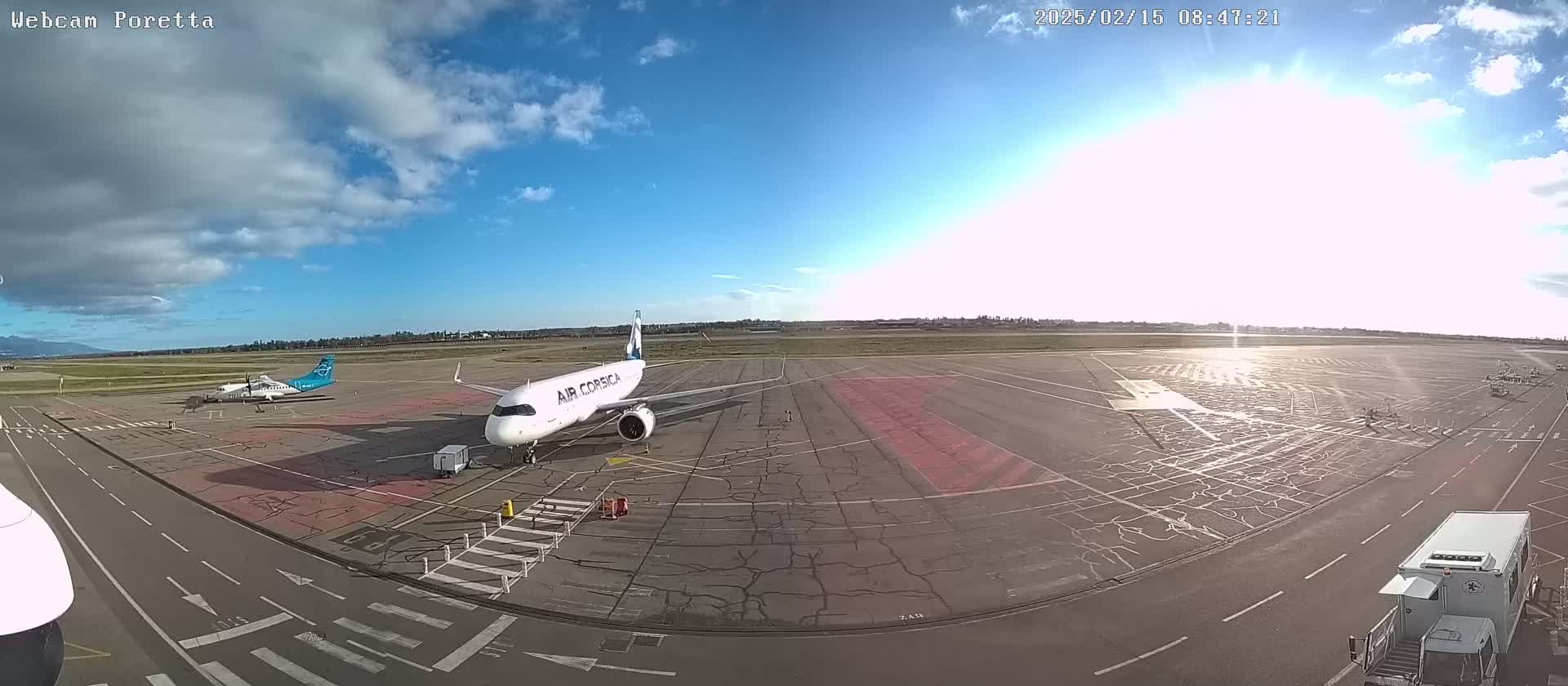 A sunny day at an airport shows two airplanes on the tarmac, one larger than the other.