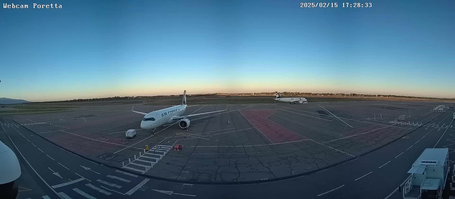 Two airplanes are parked on an airport tarmac under a clear blue sky at dusk.
