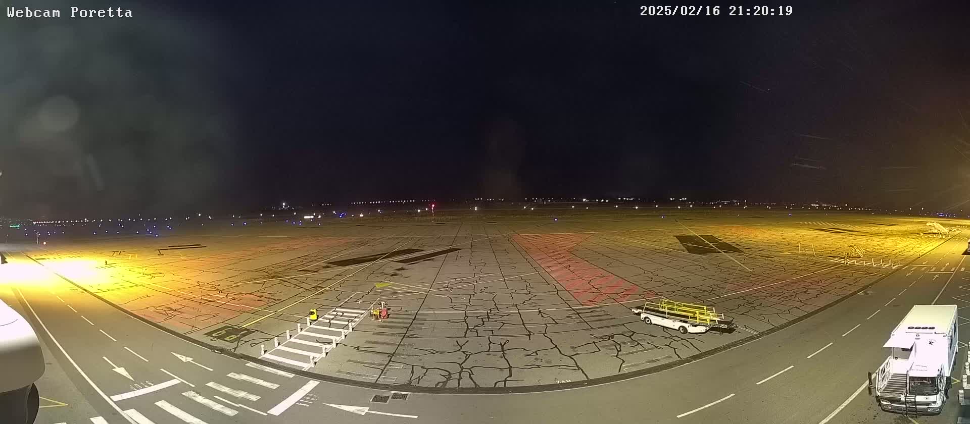 A nighttime view of an airport tarmac showing cracked pavement, some ground support equipment, and a few people, under a dark sky.