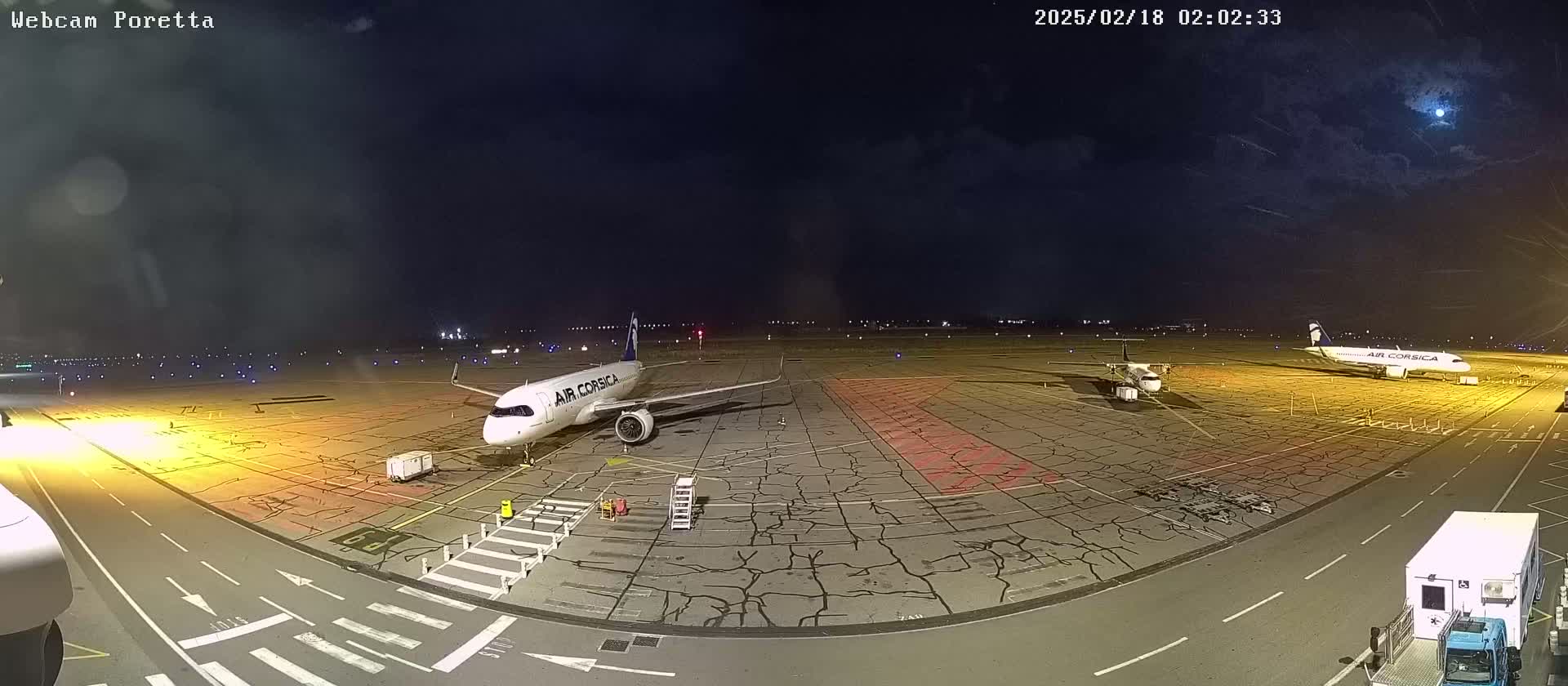 At night, under a partly cloudy sky, three airplanes are parked on an airport tarmac.